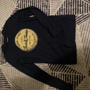 Svart långärmad tröja Jack & Jones - Svart långärmad tröja från Jack & Jones med rund hals och tryck i gult framtill. Tröjan har en klassisk passform och är tillverkad i mjuk bomull, perfekt för en chill och avslappnad stil.