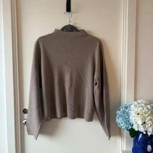 Beige stickad tröja med mock neck krage från H&M - En stilren beige stickad tröja från H&M med rak passform och lång ärm. Tröjan har en enkel design med lätt upphöjd hals och är perfekt för lager-på-lager. Mjuk och skön att bära, passar till allt i garderoben.