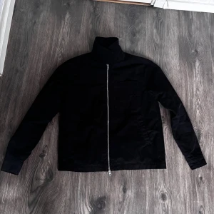 Svart jacka från New Look med dragkedja - Stilren svart jacka från New Look med hel dragkedja framtill och hög krage. Jackan har raka linjer, diskreta fickor och är tillverkad i ett slätt material. Perfekt för dig som gillar minimalistisk och clean stil.