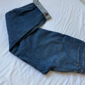 Blå jeans från Tiger of Sweden - Snygga blå jeans från Tiger of Sweden i klassisk modell med raka ben och normal passform. Jeansen har en bakficka med diskreta sömmar och är tillverkade i bomull. Perfekta för dig som gillar stilrena och tidlösa jeans.