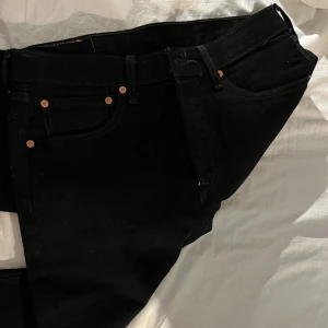 Levi's 501 jeans W31 L32 - Aldrig använda svarta Levi's 501 jeans med klassisk rak passform och fem fickor. Jeansen har kopparfärgade nitar, knappgylf och tydlig Levi's-lapp bak i midjan. Perfekta för dig som gillar tidlös stil och svart denim. 