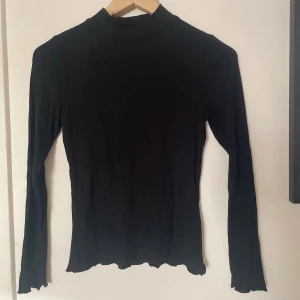Svart ribbad polotröja - Säljer en stilren svart ribbad polotröja. Den är långärmad och har en tight passform som är perfekt för höst och vinter. Tröjan är i bra skick, använd fåtal gånger🖤