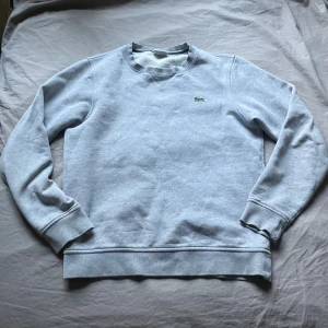 Grå sweatshirt från Lacoste Sport - Säljer en stilren grå sweatshirt från Lacoste Sport med klassisk krokodillogga på bröstet. Tröjan har rund hals, ribbade muddar och är tillverkad i mjuk bomullsblandning. Perfekt för en clean och sportig look. Storlek 3 vilket motsvarar S-M