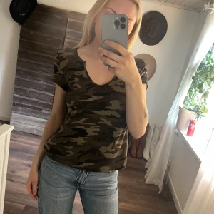 Camo t-shirt med rund hals - Snygg t-shirt med klassiskt camouflage-mönster i gröna och bruna toner. Modellen har rundad halsringning och korta ärmar, perfekt till jeans eller shorts. Mjuk och skön bomullskänsla, passar dig som gillar streetstyle.