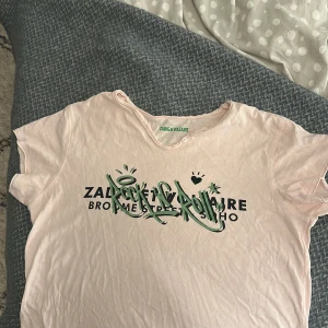 Ljusrosa t-shirt Zadig & Voltaire - Ljusrosa t-shirt från Zadig & Voltaire med coolt tryck i grönt och svart framtill. Rund halsringning med råa kanter och knappdetalj vid halsen. Skön och mjuk bomull, perfekt för en avslappnad look.