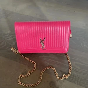 Rosa quiltad axelväska från YSL - Snygg rosa axelväska från YSL med quiltad design och guldfärgad kedja. Väskan har klassisk YSL-logga framtill, magnetlås och flera fack inuti. Perfekt för dig som vill sticka ut med en färgstark accessoar. Endast swish skickas spårbart 59kr