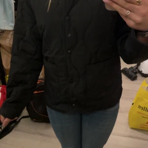 Svart quiltad jacka från H&M - Svart quiltad jacka från H&M i storlek 158. Jackan har en clean look med tryckknappar framtill, två stora fickor och vågigt quiltat mönster. Perfekt för dig som gillar en stilren och enkel vibe. Materialet är polyester och jackan är långärmad. Aldrig använd och kommer med hela paketet, passar en xs😁