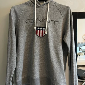 Grå hoodie från GANT  - Snygg grå hoodie från GANT . Tröjan har huva med vita snören och långa ärmar. Den har använts fåtal gånger och sedan bara legat i garderoben!