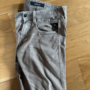Grå Replay anbass jeans med slim fit - Säljer ett par snygga grå jeans från Replay anbass med klassisk femficksdesign och svarta detaljer vid fickorna. Byxorna har en slim passform som smalnar av nedtill och är tillverkade i mjuk bomull. Perfekta för dig som gillar stilrena och bekväma jeans. Modellen är 176cm och väger 55kg