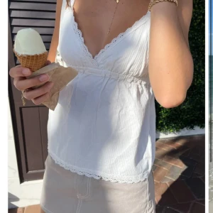 Vit spetskantad linnetopp Brandy Melville - Supersöt vit linnetopp från Brandy Melville med tunna axelband och v-ringning. Toppen har spetsdetaljer längs kanterna 🫶🏼 Nöstan aldrig använd!