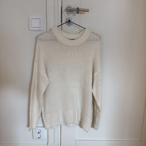 Vit stickad tröja med rund hals - Mysig vit stickad tröja med rund halsringning och långa ärmar. Tröjan har en avslappnad passform och breda ribbade muddar vid ärmslut och nederkant. Perfekt för lager-på-lager under kyliga dagar.