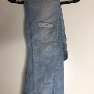 Ljusblå jeansbyxor med patchdetalj - Säljer ett par ljusblå jeansbyxor från DNM med cool patchdetalj på låret och unika sömmar vid bakfickan. Jeansen har klassisk femficksdesign och en brun läderpatch bak i midjan. Perfekta för dig som gillar en avslappnad och trendig look.