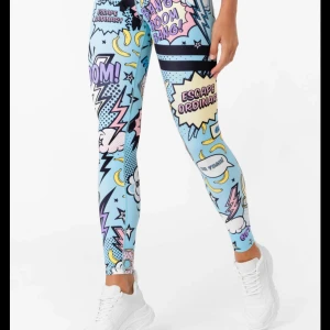 Stronger leggings med pop art-mönster - Färgglada leggings från Stronger med pop art-inspirerat tryck i blått, gult, rosa och svart. Text och motiv som blixtar, stjärnor och bananer. Hög midja och tight passform, perfekta för träning eller när du vill sticka ut.