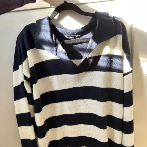 Randig finstickad tröja från Boohoo - Säljer en finstickad tröja från Boohoo med breda marinblå och vita ränder. Tröjan har v-ringning med krage, långa ärmar och en loose passform. Perfekt för dig som gillar en chill och stilren look. Den är något nopprig, men det kan säkert gå bort med noppbortagare ☺️
