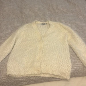 Vit fluffig kofta med knappar - Supermjuk och fluffig vit kofta från Kappahl . Koftan har lång ärm och en mysig, stickad känsla som passar perfekt när det är kallt. Enkel och stilren design som är lätt att matcha med allt.