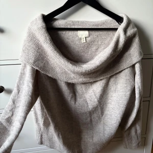 Beige stickad tröja från H&M - Supermysig beige stickad tröja från H&M med bred, nedvikt krage och lång ärm. Perfekt för lager-på-lager och chill höst- eller vinterstil. Ribbstickade detaljer vid krage, ärmslut och nederkant ger extra stilpoäng.