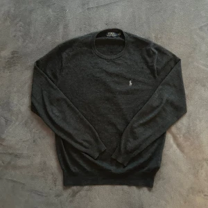 Mörkgrå Ralph lauren merinoull sweatshirt - En mörkgrå ralph lauren sweatshirt i merinoull. Tröjan är i utmärkt skick förutom ett litet hål som man kan se på bild 5, men det är inget man märker av när man har på tröjan. Tröjan är i storlek medium.