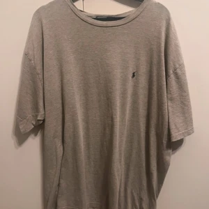 Grå  t-shirt från Polo Ralph Lauren XL - En stilren grå  t-shirt från Polo Ralph Lauren i storlek XL. T-shirten har klassisk passform, korta ärmar och den ikoniska lilla broderade loggan på bröstet. Tillverkad i mjuk bomull som känns skön mot huden. Perfekt till jeans eller shorts. 