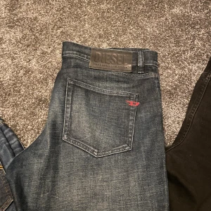 Mörkblå jeans från Diesel - Snygga mörkblå jeans från Diesel med klassisk femficksdesign och diskreta slitningar. Jeansen har en läderpatch med Diesel-logga bak i midjan och en liten röd detalj på bakfickan. Materialet är robust denim i bomull.