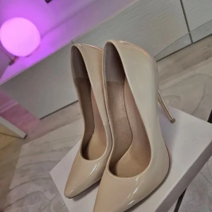 Klackar  - Stilrena pumps i beige lack från Simmi London. De har ett fint skick, hög klack och en glansig finish med en elegant känsla. Perfekt för dig som vill sticka ut med en klassisk och trendig look. Använd endast en gång i nyskick. 