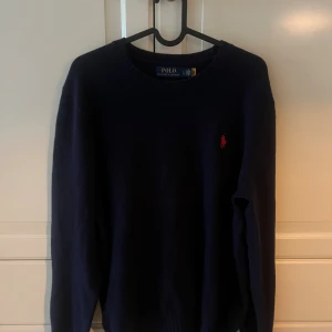 Mörkblå stickad Kashmir tröja Polo Ralph Lauren - Klassisk mörkblå stickad kashmir tröja från Polo Ralph Lauren med rund halsringning och röd broderad logga på bröstet. Perfekt för dig som gillar stilrena och tidlösa plagg. Långärmad och mjuk, passar till allt. använd en gång, Pris kan diskuteras.