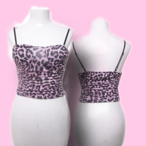 Lila leopardmönstrad linnetopp - Säljer en lila och svart leopardmönstrad linnetopp från New Collection. Toppen har smala svarta axelband, rynkade sidor och figurnära passform. Materialet är stretchigt och glansigt, perfekt för en trendig look.