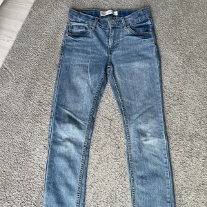 Levi's 510 ljusblå skinny jeans 12A - Snygga Levi's 510 skinny jeans i ljusblå tvätt med klassiska fem fickor och gul kontrastsöm. Jeansen har en smal passform och är tillverkade i en mjuk bomullsblandning med lite stretch för extra komfort. Perfekta för dig som gillar en modern och slimmad look.