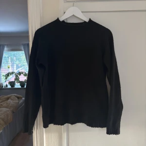 Svart stickad tröja  - En enkel svart stickad tröja med en lite högre hals och långa ärmar. Perfekt att slänga på sig när det är kyligt ute. Tröjan har en klassisk passform och ribbade muddar vid ärmslut och nederkant.