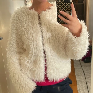Vit fluffig pälsjacka - Säljer en supermjuk och fluffig vit pälsjacka med lång ärm. Jackan har en kortare, boxig passform och är perfekt för dig som vill sticka ut med en cozy vibe. Ingen synlig knäppning framtill och riktigt skön att bära under kyliga dagar.