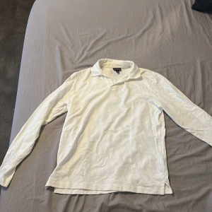 Vit långärmad topp från H&M - Klassisk vit långärmad topp från H&M med krage och mjukt material. Perfekt till jeans eller kjol för en clean och enkel look. Passar dig som gillar stilrena plagg med en avslappnad känsla.