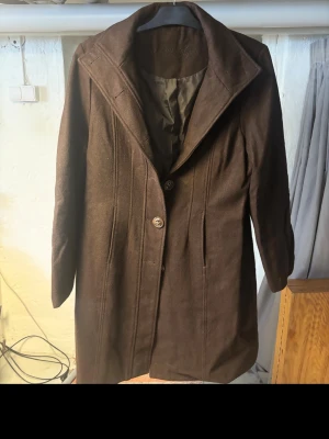 Brun kappa från Marie Philippe - Snygg brun kappa från Marie Philippe med klassisk krage och två knappar framtill. Jackan har en stilren design med diskreta sömmar och är helfodrad på insidan. Perfekt för dig som gillar en elegant och tidlös look.