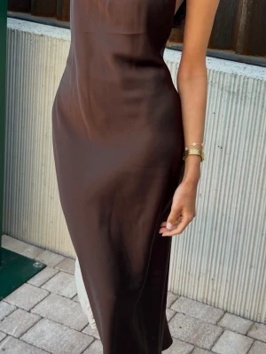 Brun satinklänning med halterneck - Elegant brun långklänning i satin med halterneck och knyt i nacken. Öppen bak. 