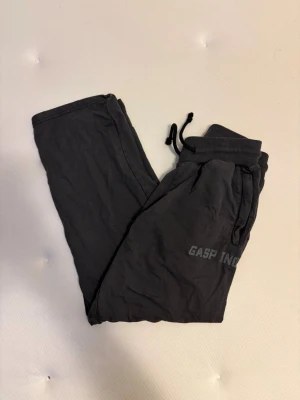 Svarta mjukisbyxor från GASP INC - Säljer ett par svarta mjukisbyxor från GASP INC med dragsko i midjan och ribbade muddar. Byxorna har fickor med dragkedja och tryckt logga på benet. Perfekta för chill eller gymmet. 