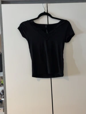 Svart spetsdetaljerad topp XS - Använd 2 gånger.Säljer en svart topp från The Black Label Collection i storlek XS. Toppen har v-ringning med fina spetsdetaljer längs halsen och korta ärmar. Materialet känns mjukt och stretchigt, perfekt till många olika looks.