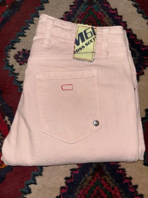 Ljusrosa Miss Sixty jeans Eden - Säljer ett par ljusrosa jeans från Miss Sixty, modell Eden. Byxorna har låg midja, raka ben och klassiska femficksdetaljer med silverfärgade nitar. Materialet är mjuk bomull med en hint av stretch för extra komfort.
