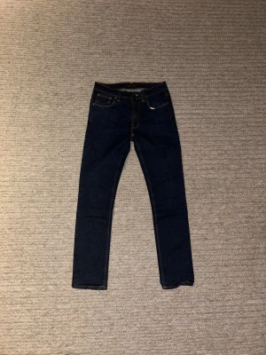 Mörkblå Nudie Jeans  - Snygga mörkblå jeans från Nudie Jeans i modellen Lean Dean. Jeansen har en smalare passform och är smalare än andra jeans i storlek 31. Tillverkade i slitstarkt bomullsmaterialoch är perfekt för dig som gillar en stilren och modern look.