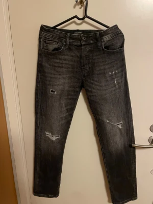 Jack & Jones jeans - Säljer ett par svarta skinny jeans från Jack & Jones med slitna detaljer och snygg tvätt. Jeansen har fem fickor, låg midja och smal passform som sitter tajt längs benen. Perfekt för dig som gillar en cool och modern stil.