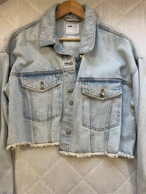 Ljusblå croppad jeansjacka F3 Sister - New Yorker  - Säljer en ljusblå croppad jeansjacka från F3 Sister. Jackan har rå kant nertill, två bröstfickor med knappar och klassisk krage. Perfekt för dig som gillar en avslappnad och trendig stil.