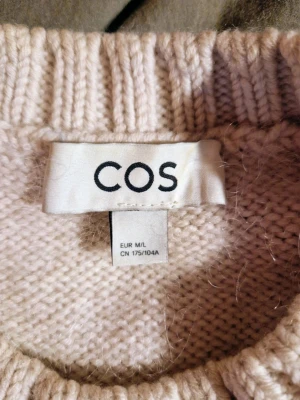 Beige stickad tröja från COS M/L  - Säljer en beige cremevit stickad tröja från COS i storlek M/L. Tröjan har en chunky struktur med rutmönster, ribbade muddar och rund hals. Materialet är en mix av ull och mohair som gör den extra mjuk och fluffig. Perfekt för kyliga dagar.
