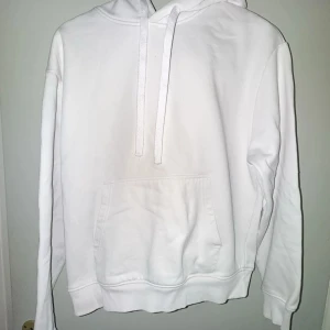 Vit hoodie med huva från Zara - Säljer en stilren vit hoodie med huva och snörning. Tröjan har en klassisk känguruficka framtill och ribbade muddar vid ärmslut och nederkant. Perfekt för dig som gillar enkel och clean streetstyle. Passar dig som vill ha en basic och bekväm look.