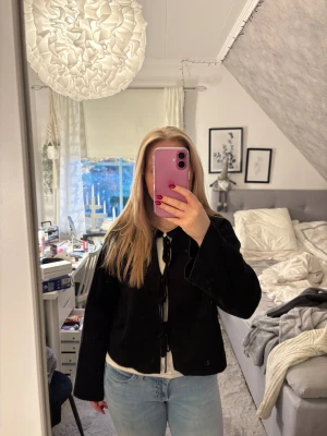 Svart kofta med snörning framtill - Säljer en svart kofta med snygg snörning framtill. Koftan har lång ärm och är i ett mjukt, lite tjockare material som känns skönt mot huden. Perfekt att slänga över en topp eller t-shirt för en chill look.