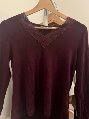 Vinröd intimissimi liknande topp - Säljer en vinröd långärmad topp från Gina Tricot med snygg spetsdetalj runt v-ringad hals. Toppen har en slim passform och är gjord i mjukt material som känns skönt mot huden. Perfekt att styla med jeans eller kjol för en cool look.