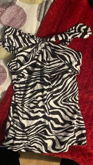 Zebramönstrad oneshoulder topp SHEIN - Säljer en snygg zebramönstrad topp från SHEIN i oneshoulder-modell. Toppen är svartvit med bred axel arrangements och stretchigt material som sitter bekvämt. Perfekt för dig som vill sticka ut med ett djurmönster.