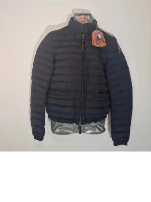 Mörkblå pufferjacka från Parajumpers - Säljer en mörkblå pufferjacka från Parajumpers med hög krage och dragkedja framtill. Jackan har quiltad design, två fickor och klassisk logga på ärmen. Perfekt för kyliga dagar och riktigt snygg till jeans eller hoodie.