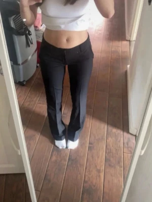 Svarta bootcut kostymbyxor - Säljer ett par svarta kostymbyxor med bootcut passform och hög midja. Byxorna har klassisk look med raka ben som blir vidare nedtill och stängs med knapp och dragkedja. Perfekta till en snygg och clean outfit.
