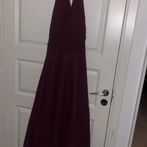 Lila balklänning - Säljer en lila långklänning från Andiamo med halterneck och v-ringad front. Öppen i ryggen. Klänningen har ett elegant fall och är tillverkad i ett glansigt material som ger en lyxig känsla. Perfekt nu inför vårens studentbal/lärarmiddag 🤍Använd 1 gång, mammas gamla därav har jag inga passformsbilder. Står att det är storlek 40 men mer som 38. Längd ca 164-170cm