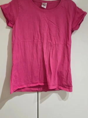 Rosa t-shirt från Fruit of the Loom - Säljer en rosa t-shirt från Fruit of the Loom, modell Lady Fit Valueweight. T-shirten har rund hals och korta ärmar, perfekt för dig som gillar enkel och färgstark stil. Materialet är mjuk bomull som känns skönt mot huden.