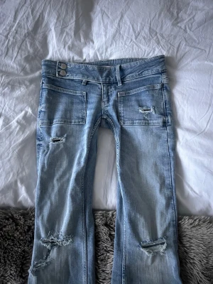 Bootcut jeans från Gina Tricot, ljusblå - Säljer ett par ljusblå bootcut jeans från Gina Tricot i storlek S. De har låg midja, slitna detaljer och stora fickor fram. Har aldrig använt jeansen men har spretat upp dom nertill 💕💕