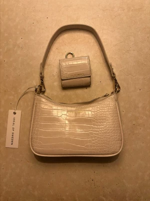 Beige handväska fårn ideal of sweden - Snygg beige väska från Ideal of Sweden med krokodilpräglat mönster och guldfärgade detaljer. Väskan är aldrig använd och det lilla tillhörande fodralet ingår i priset💕💕