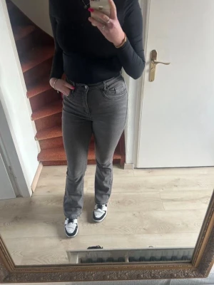 Grå bootcut jeans med hög midja - Snygga grå jeans med bootcut-snitt och hög midja. Jeansen har klassisk femficksdesign, dragkedja och knapp framtill. Materialet är jeans med en lätt tvättad look som ger en cool vibe. Passar dig som gillar en stilren och trendig look.